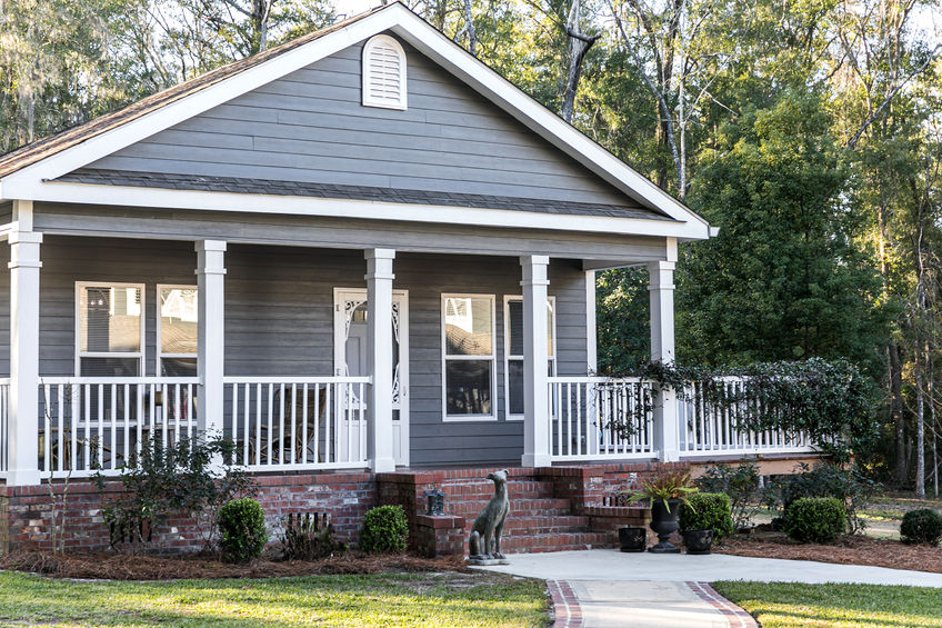 Close-up of small blue gray in-law suite home with a front and side porch with white railing.